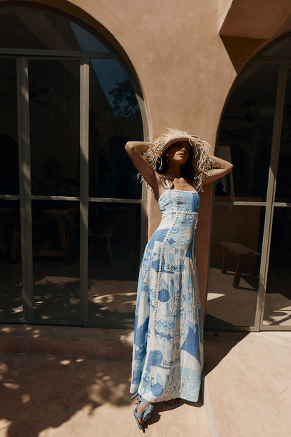 Full length view of a model in a straw hat wearing the blue porcelain print maxi dress in the sun