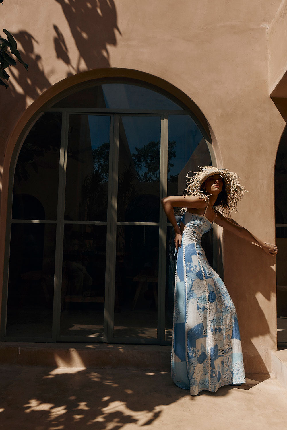Model leaning against a terracotta wall in the blue porcelain print maxi dress