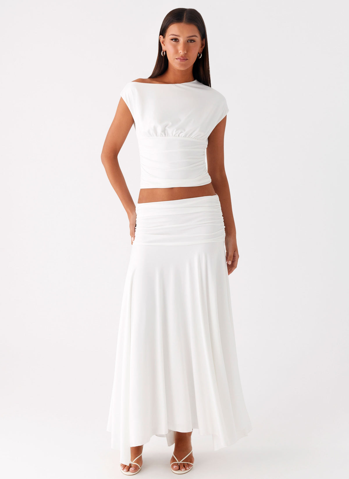 Model wearing a white low-rise ruched maxi skirt with a flared hem and matching cap sleeve top