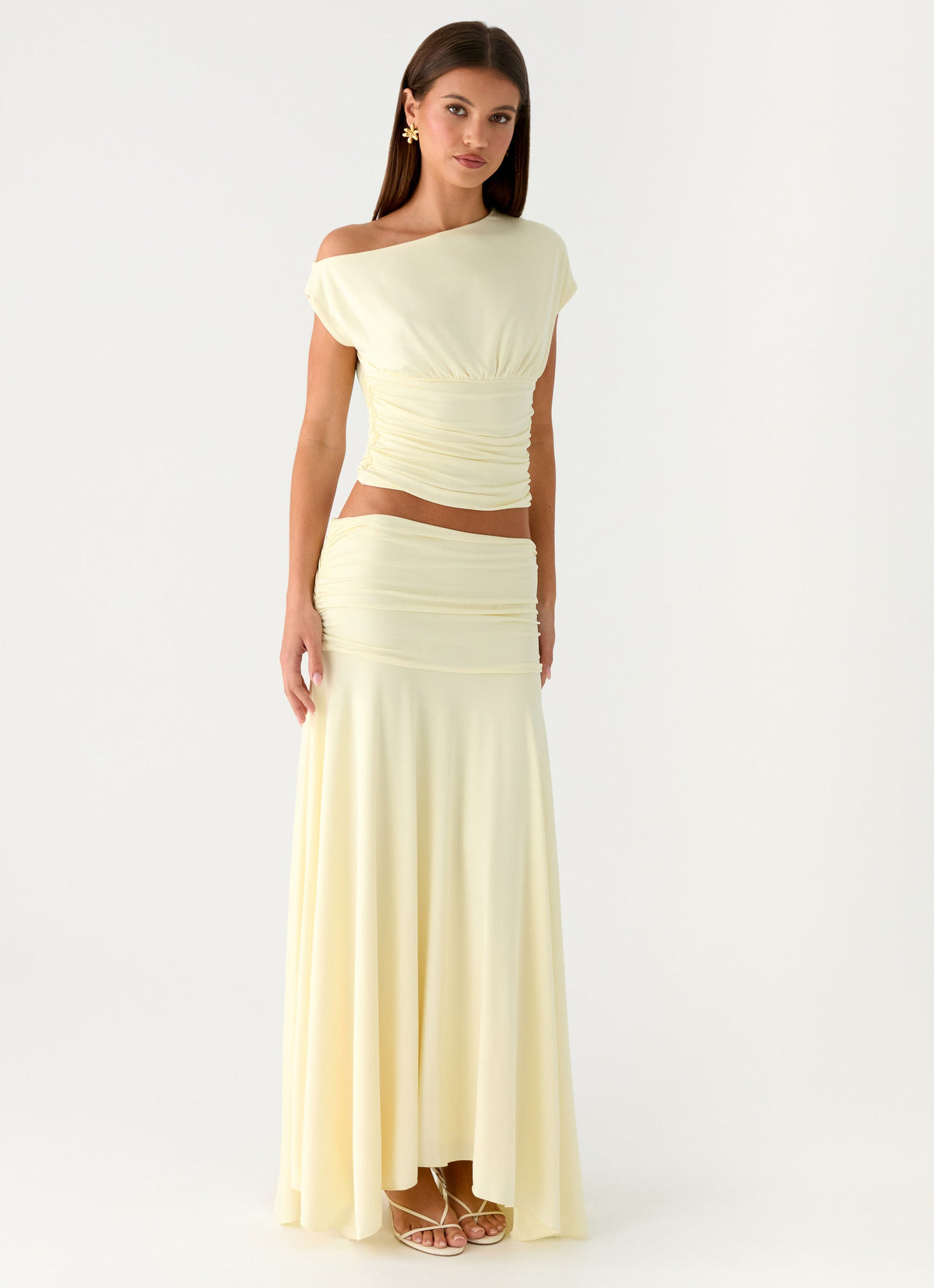 Model wearing a pale yellow low-rise ruched maxi skirt with a flared hem and matching top