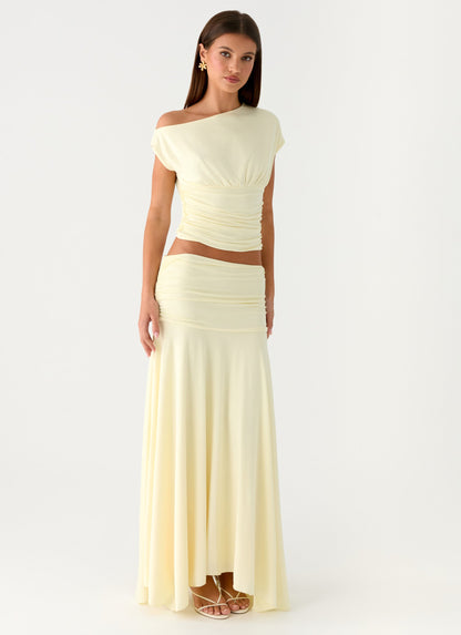 Model wearing a pale yellow low-rise ruched maxi skirt with a flared hem and matching top