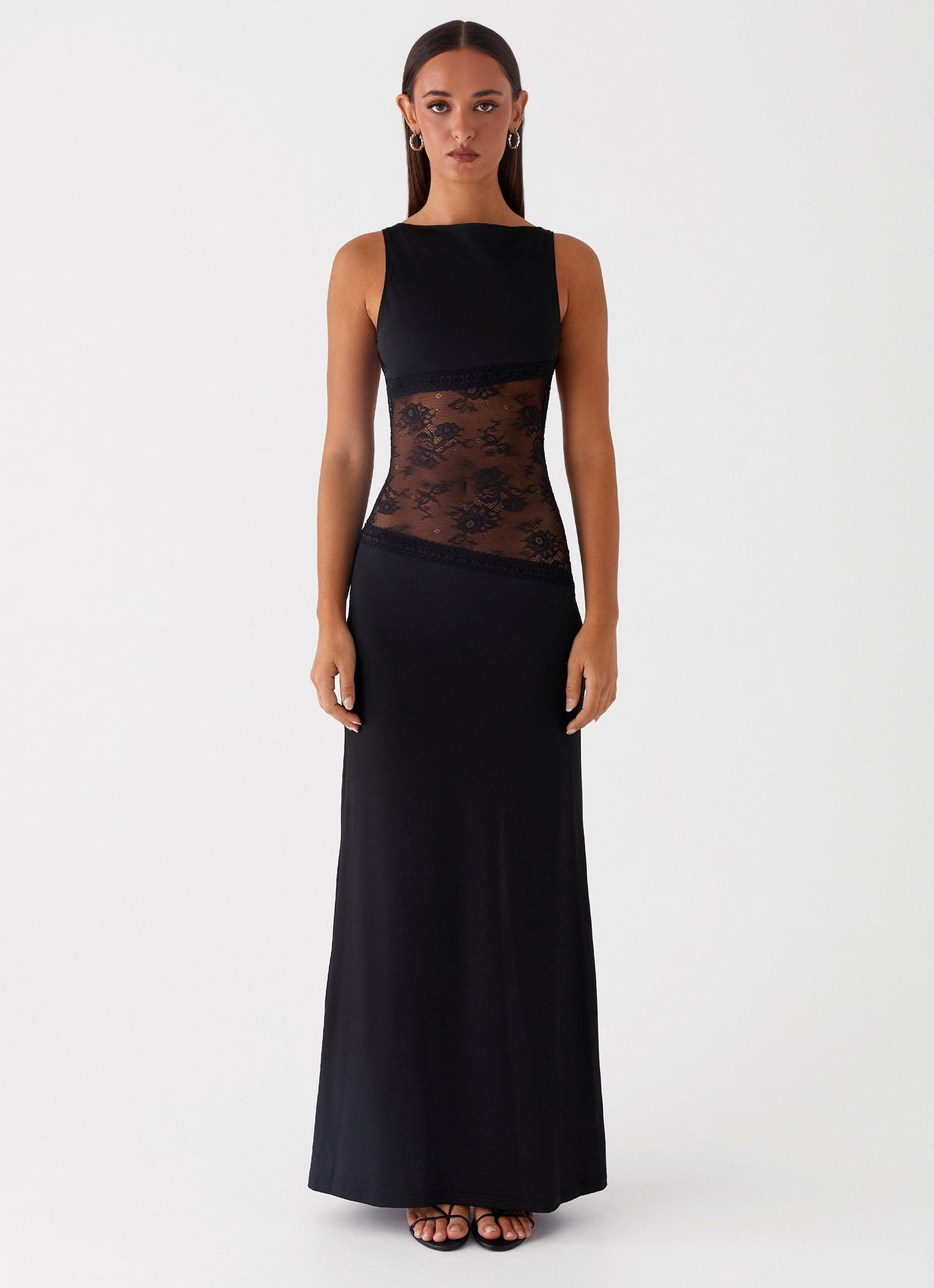 Model wearing a black jersey maxi dress with a high round neck and a diagonal sheer black lace waist panel