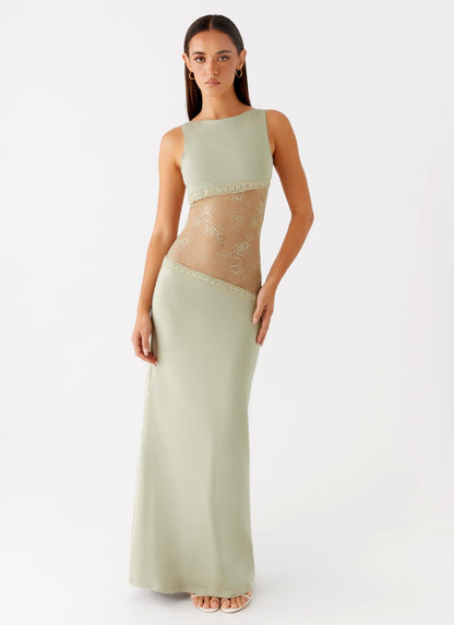 Model wearing a sage green jersey maxi dress with a high round neck and a diagonal sheer lace waist panel