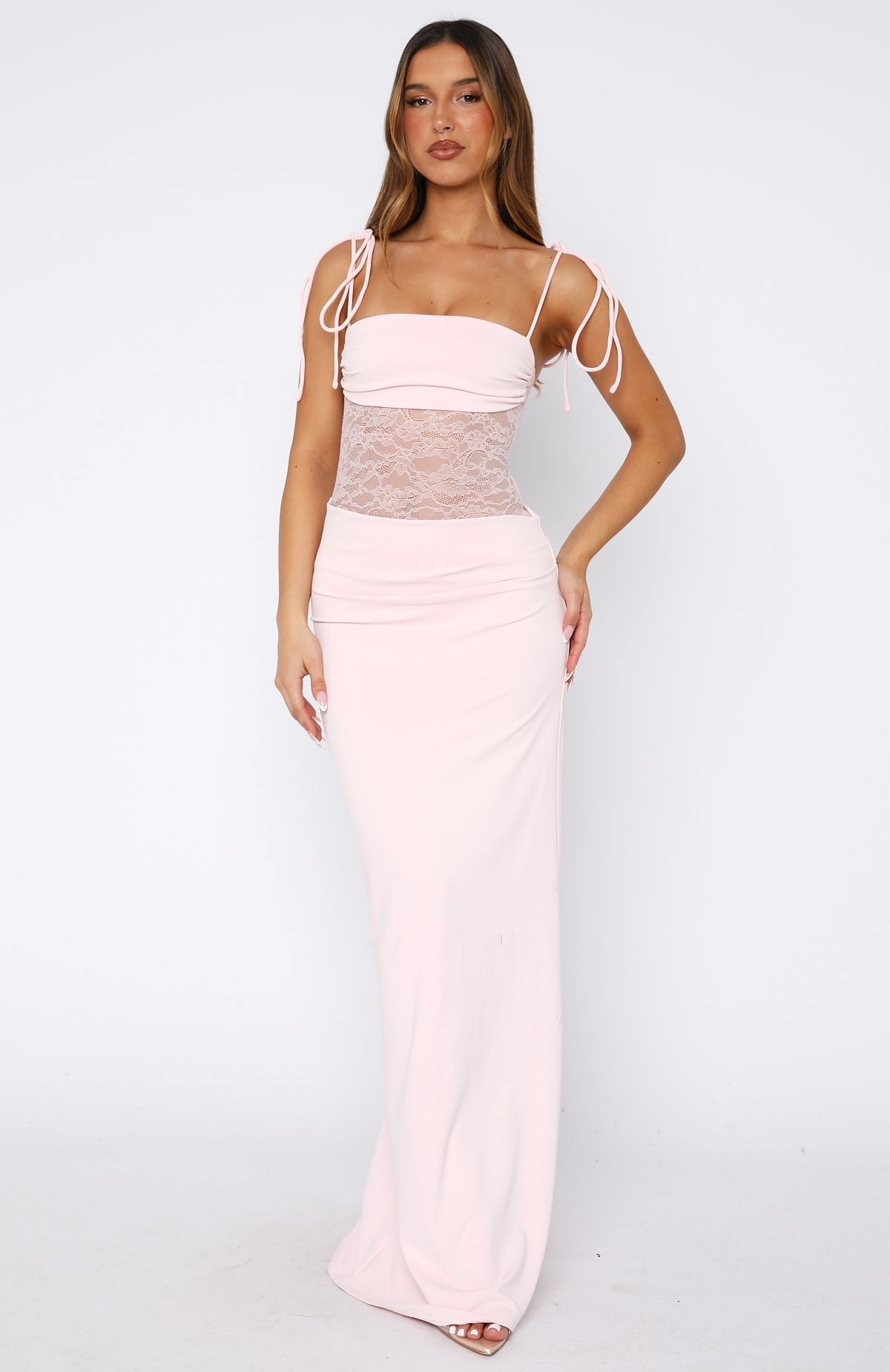 Model wearing a baby pink stretch maxi dress with a sheer lace bodice, square neck and thin tie straps