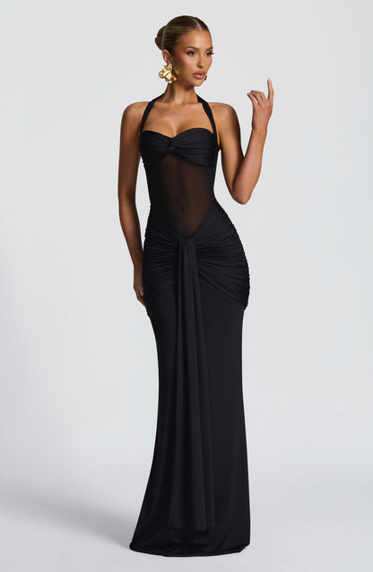 Model wearing a black slinky maxi dress with a sweetheart twist bust, halter ties and sheer mesh midriff