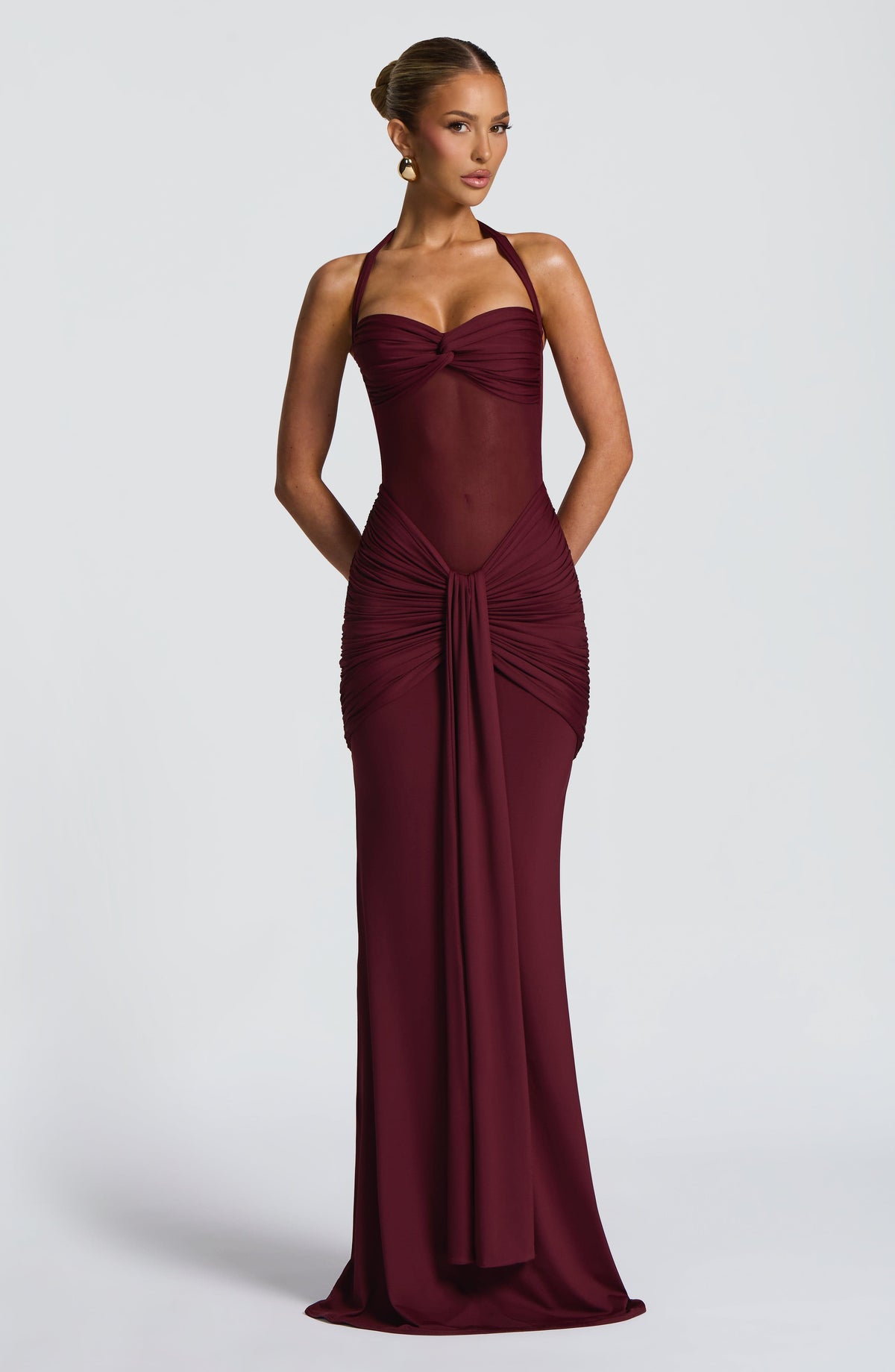 Model wearing a deep cherry red maxi dress with a sweetheart twist bust and sheer mesh midriff