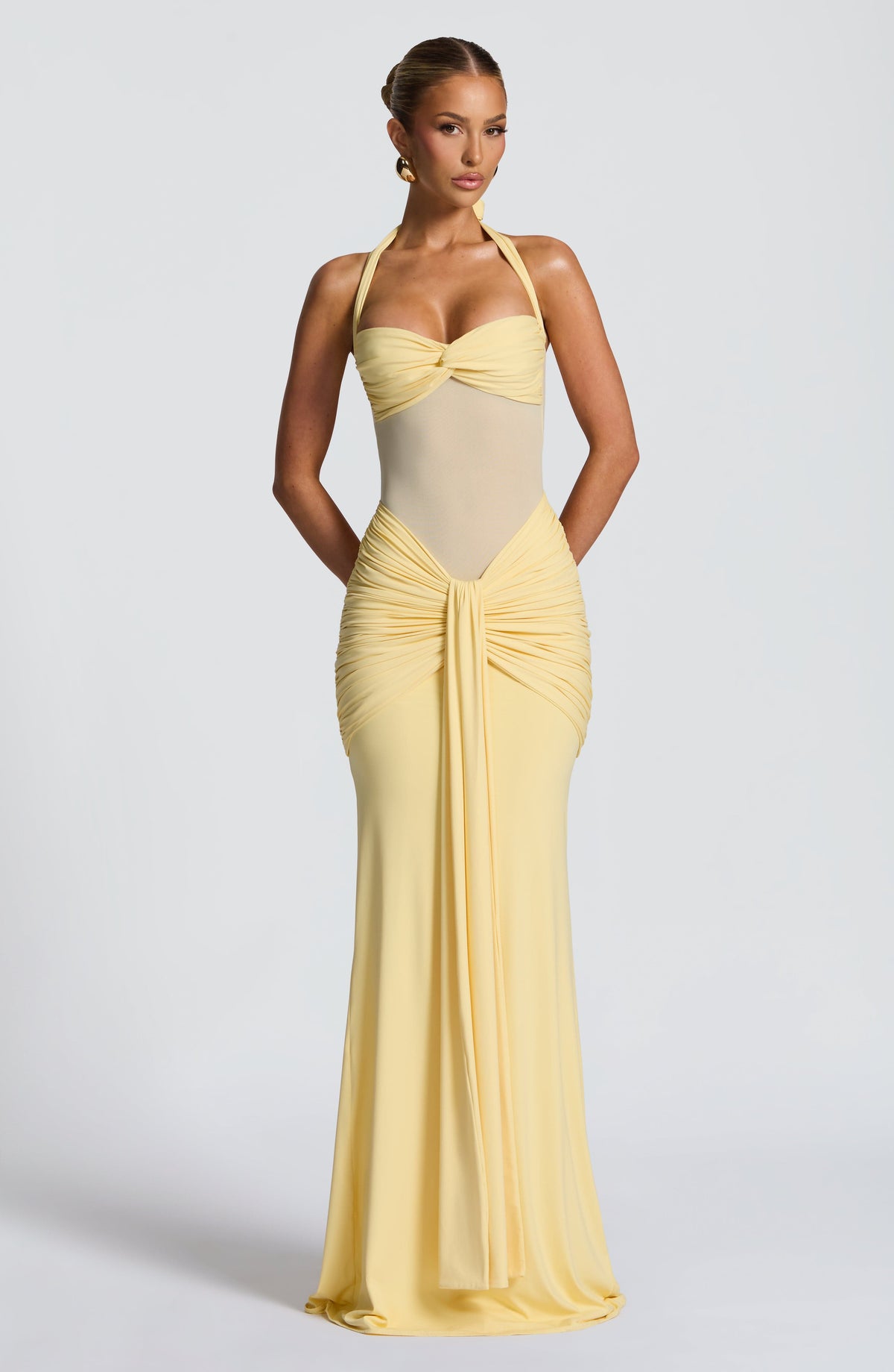 Model wearing a pale lemon maxi dress with a sweetheart twist bust, halter ties and sheer mesh midriff