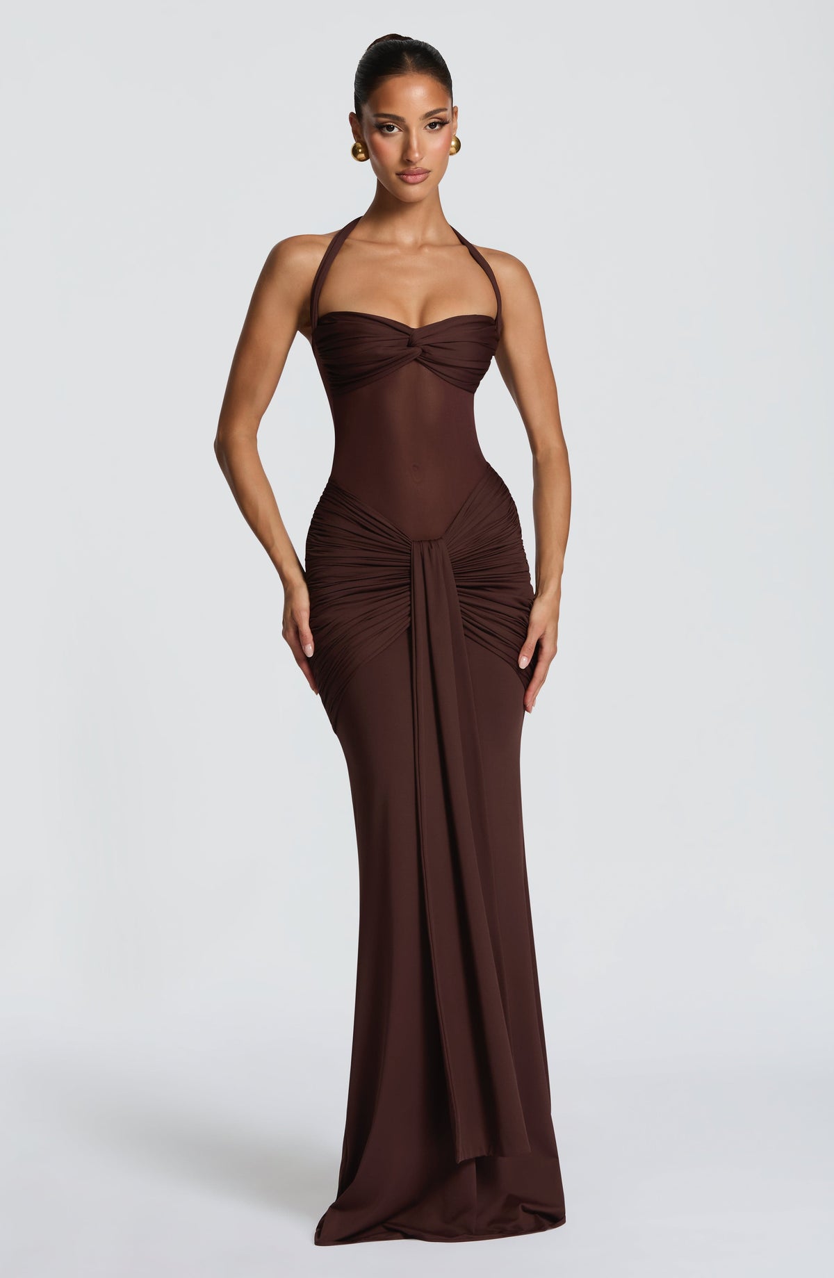 Model wearing a plum brown maxi dress with a sweetheart twist bust, halter ties and sheer mesh midriff