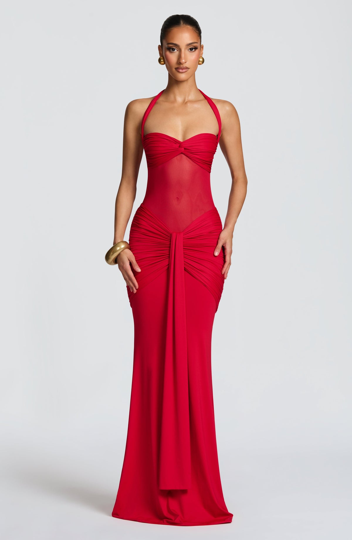 Model wearing a red slinky maxi dress with a sweetheart twist bust, halter ties and sheer mesh midriff