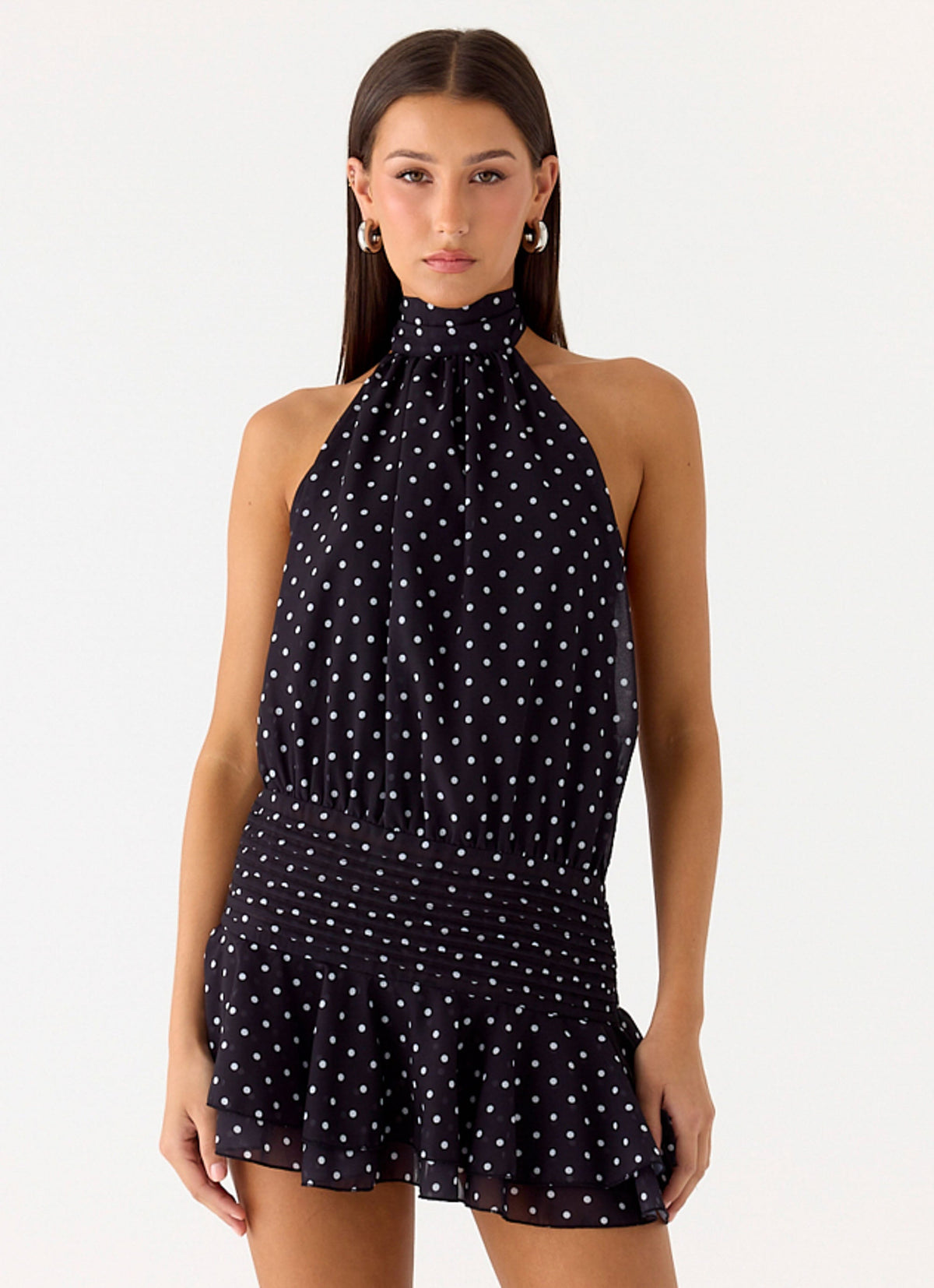 Model wearing a black chiffon halter mini dress with white polka dots and a pleated drop waist