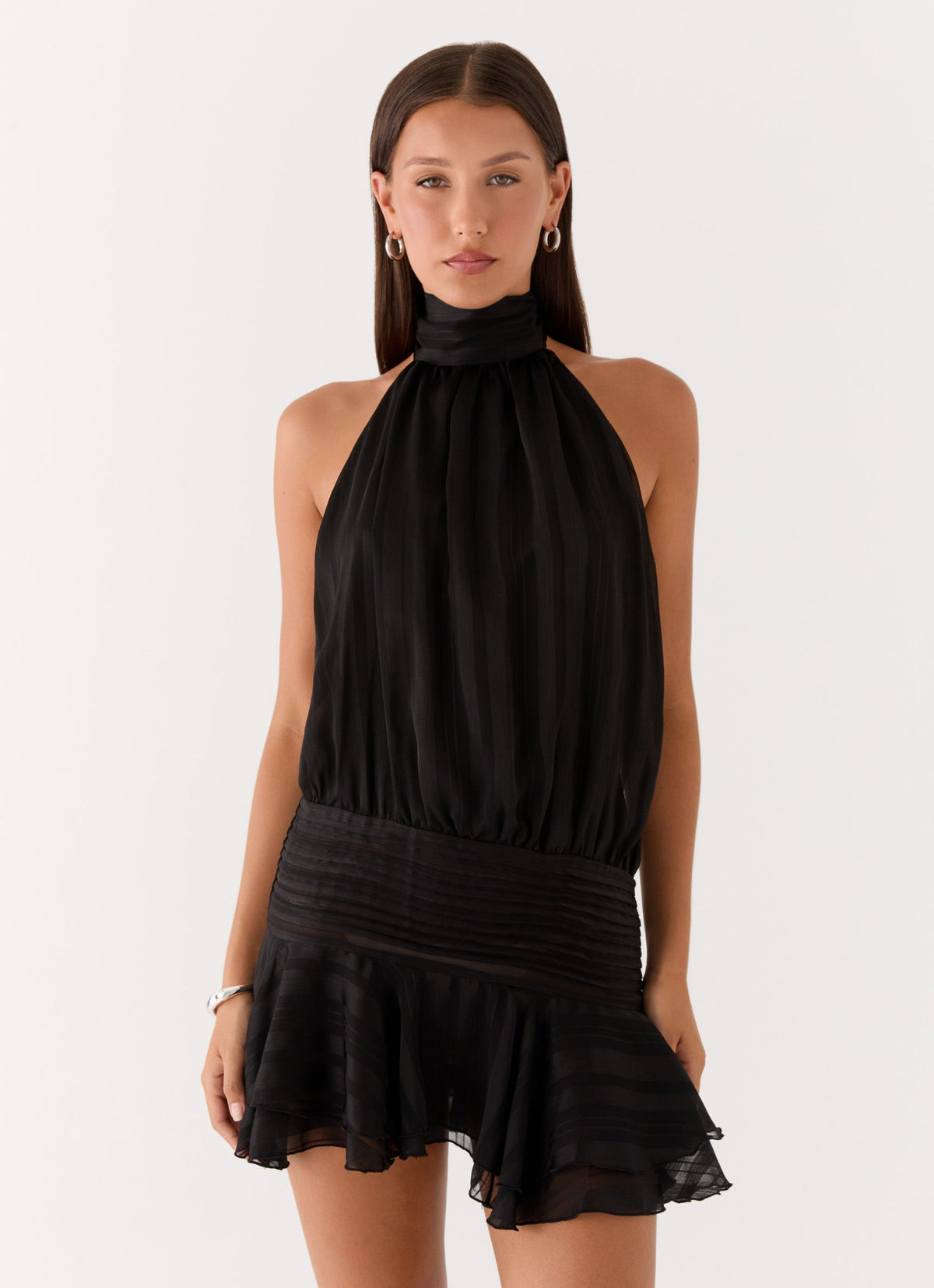 Model wearing a black chiffon halter neck mini dress with a pleated drop waist and tiered flared hem