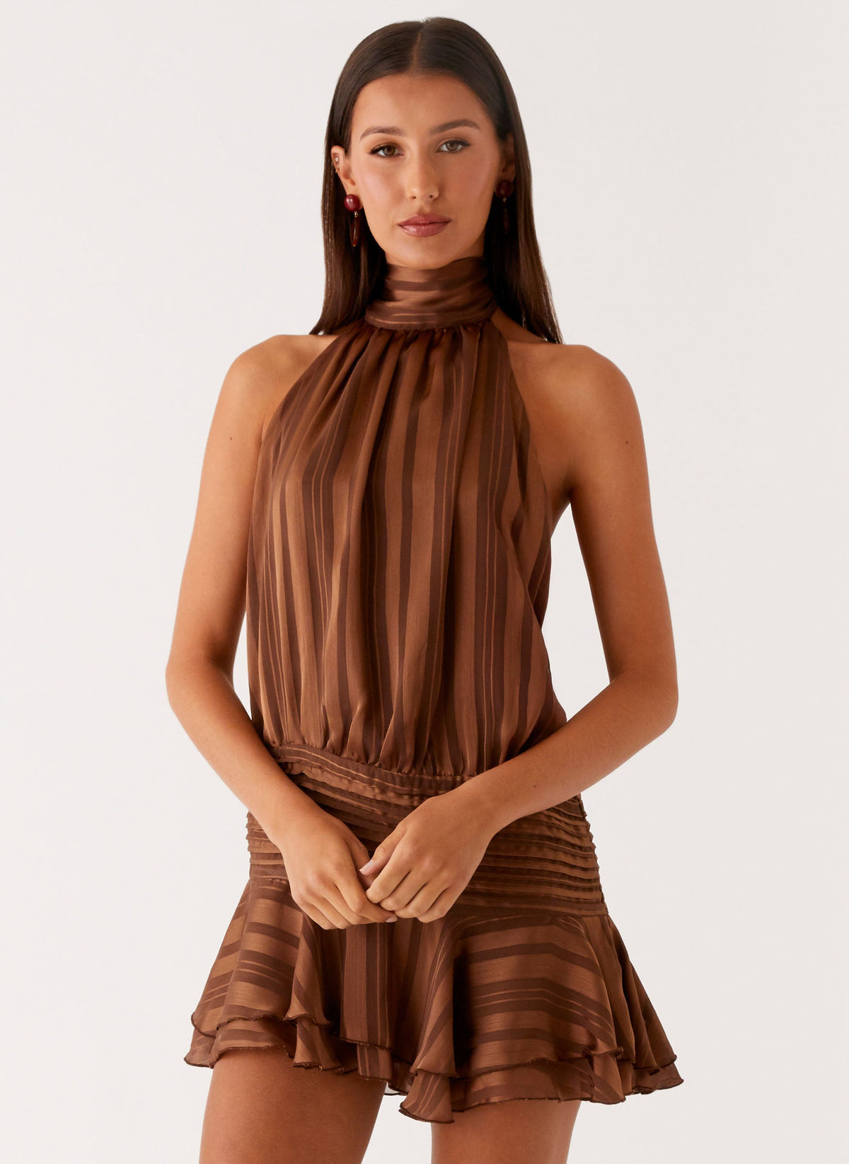 Model wearing a chocolate brown chiffon halter neck mini dress with a pleated drop waist and flared hem
