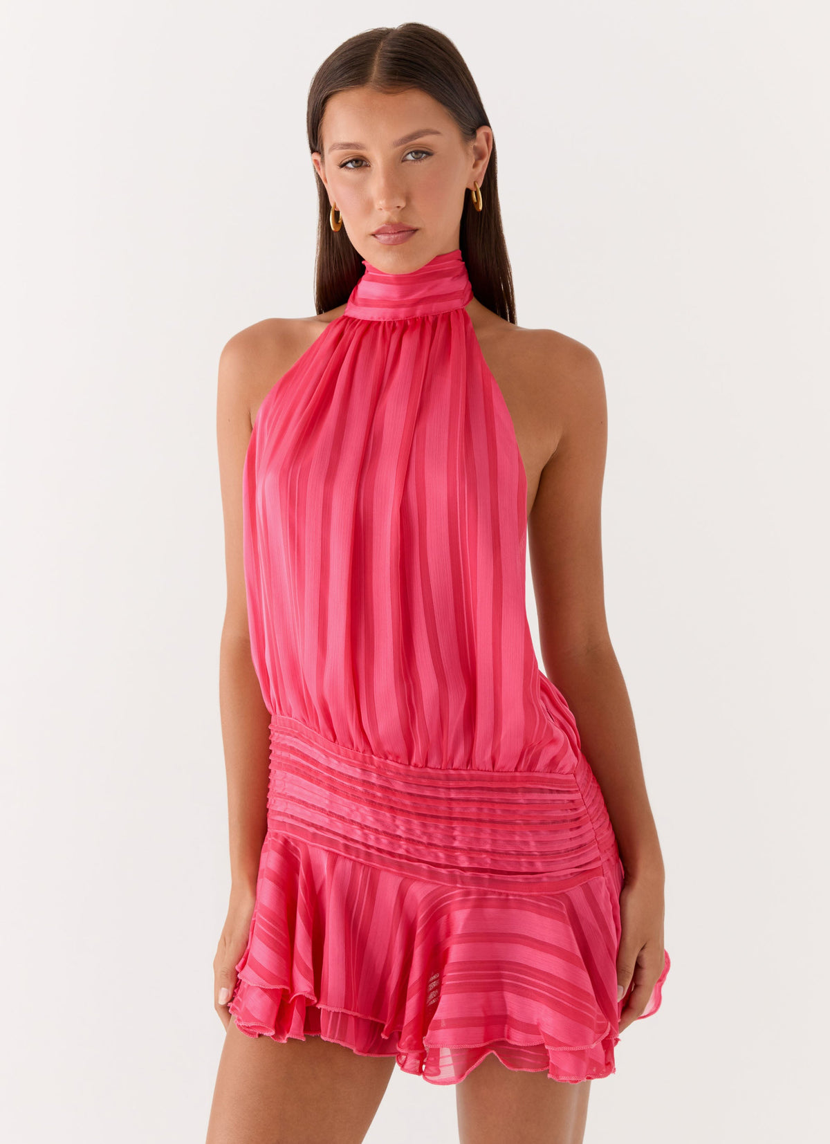 Model wearing a fuchsia pink chiffon halter neck mini dress with a pleated drop waist and flared hem