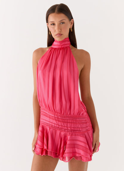 Model wearing a fuchsia pink chiffon halter neck mini dress with a pleated drop waist and flared hem