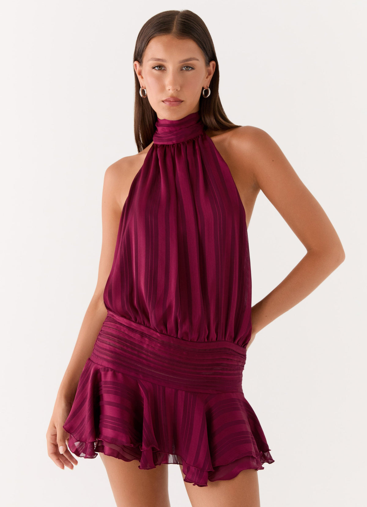 Model wearing a plum chiffon halter neck mini dress with a pleated drop waist and tiered flared hem