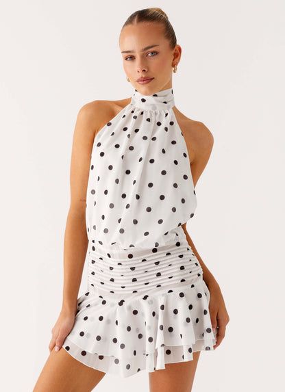 Model wearing a white chiffon halter mini dress with black polka dots and a pleated drop waist