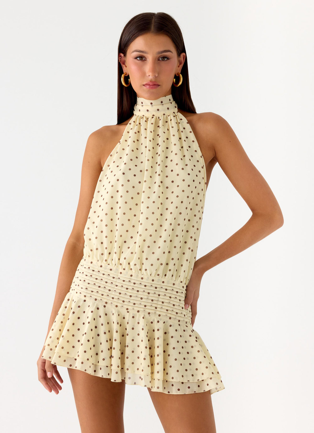 Model wearing a pale yellow chiffon halter mini dress with polka dots and a pleated drop waist