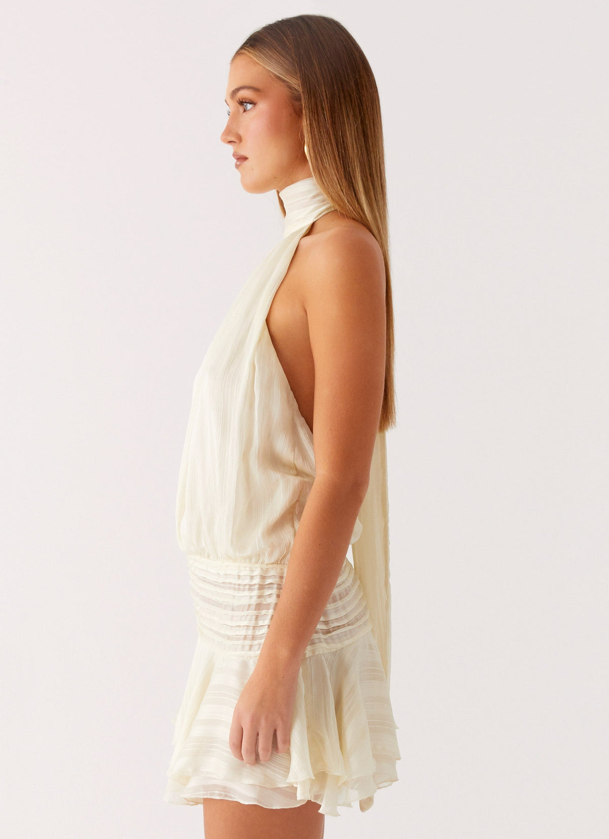 Side view of the ivory chiffon halter neck mini dress showing the drop waist and flared hem